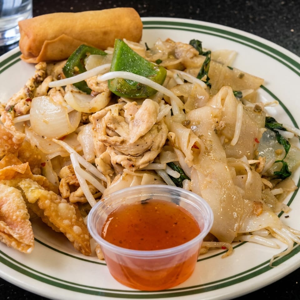 Plate of stir-fried noodles with chicken, vegetables, crispy wontons, a spring roll, and sweet chili sauce.